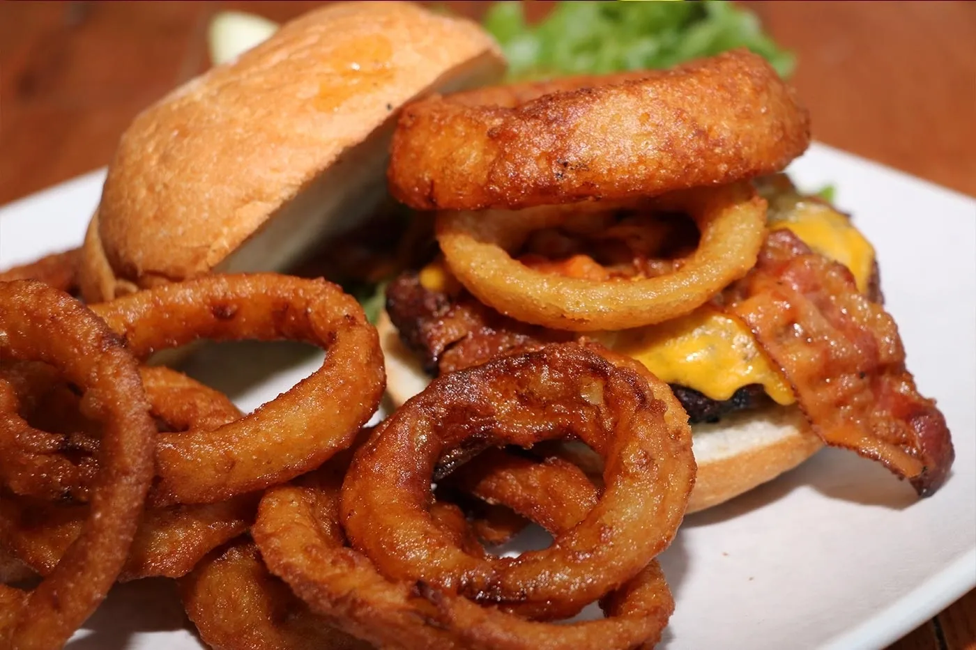 A burger with bacon and onion rings on a plate.