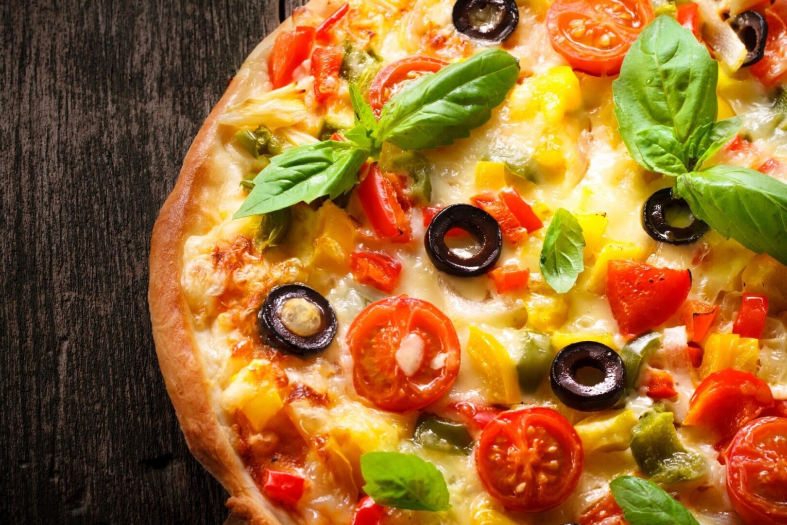 A pizza with tomatoes, olives, and basil on a wooden table.