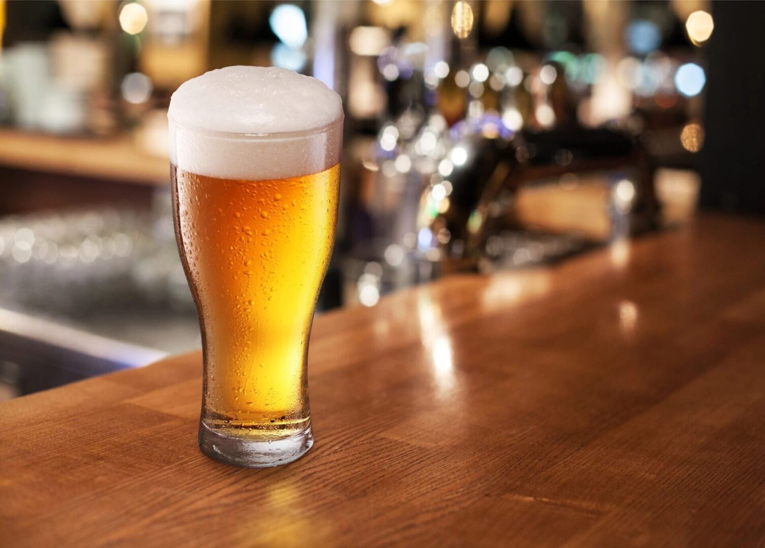 A glass of beer sitting on a wooden bar.