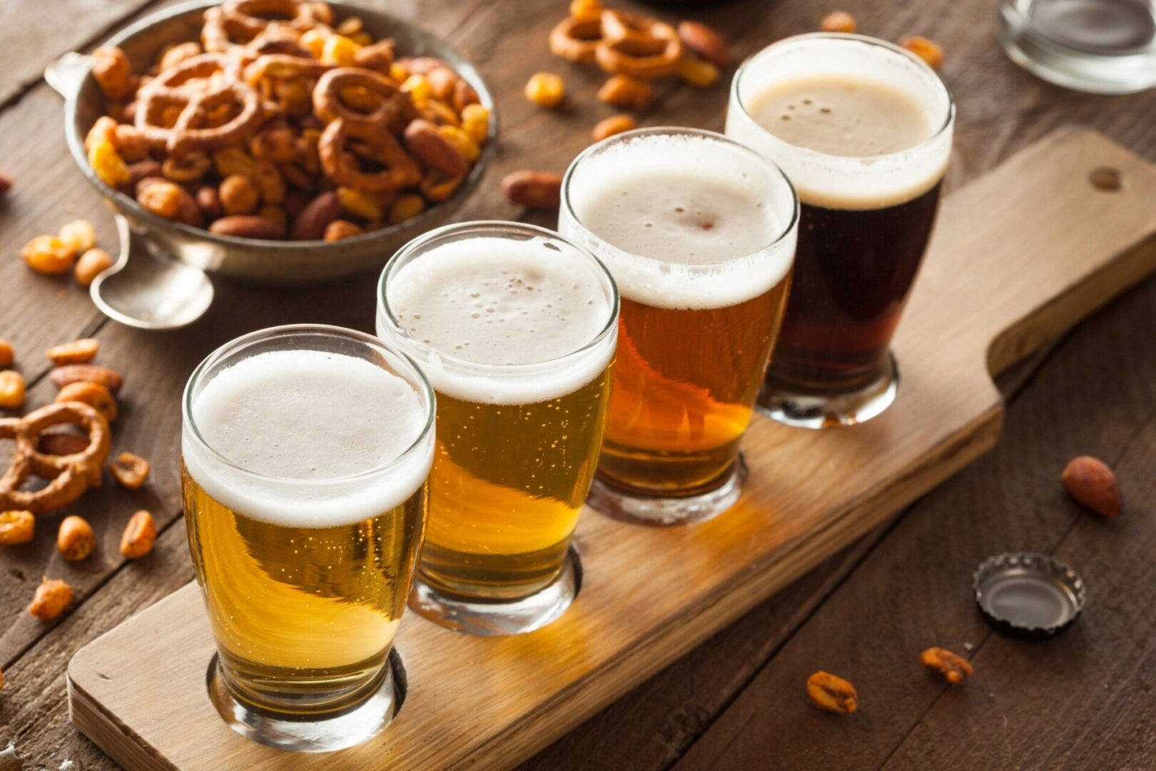 Four glasses of beer and pretzels on a wooden board.