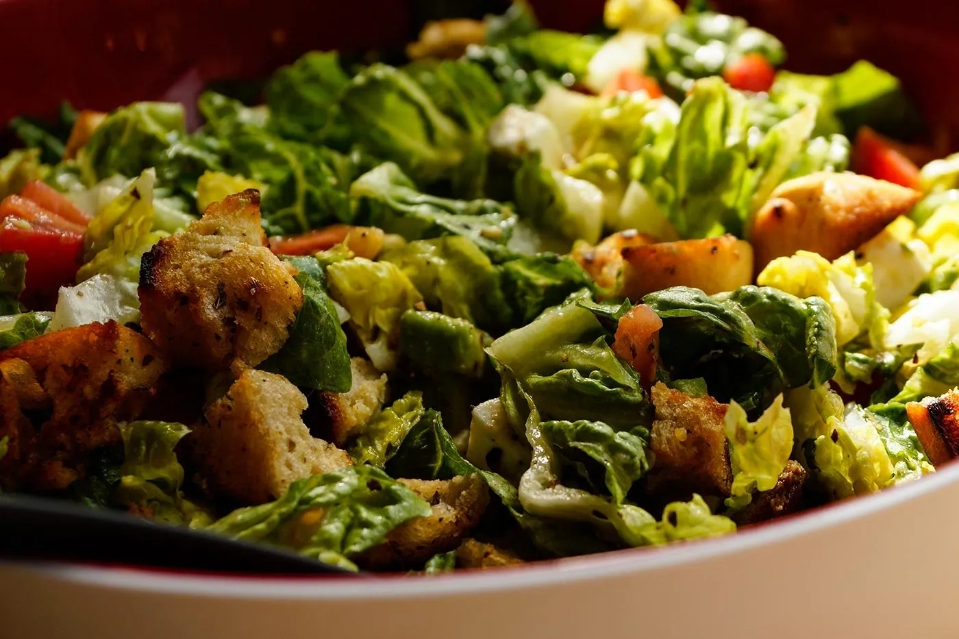 A bowl of salad with croutons and tomatoes.